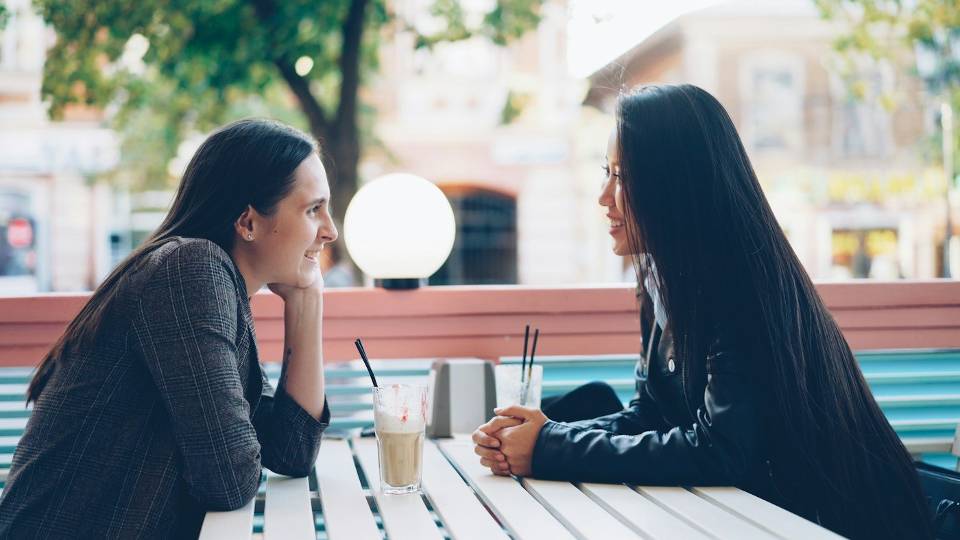 Two women talking across an outdoor café table