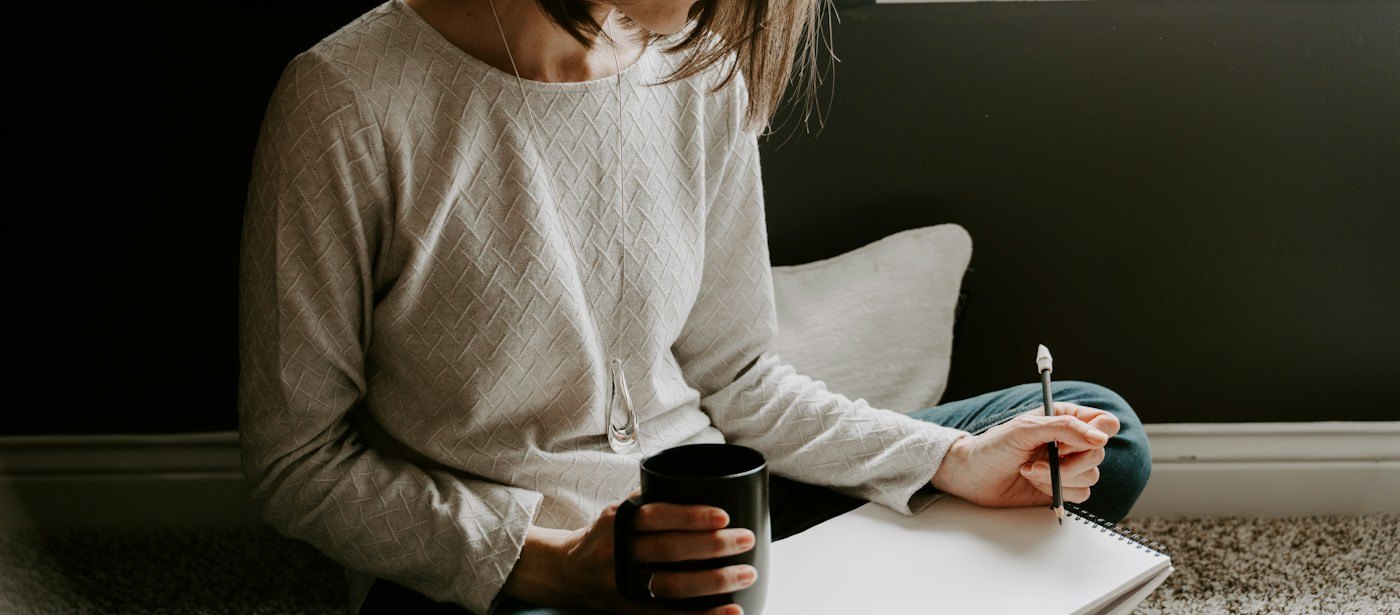 Woman writing in a notebook with a cup of coffee nearby